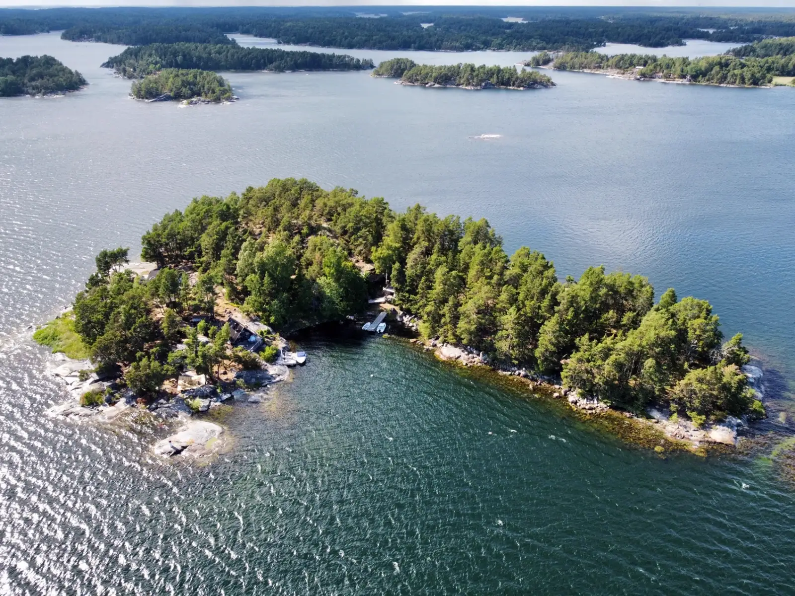 Drönarbild över ö med bostäder omgivna av vatten och skog